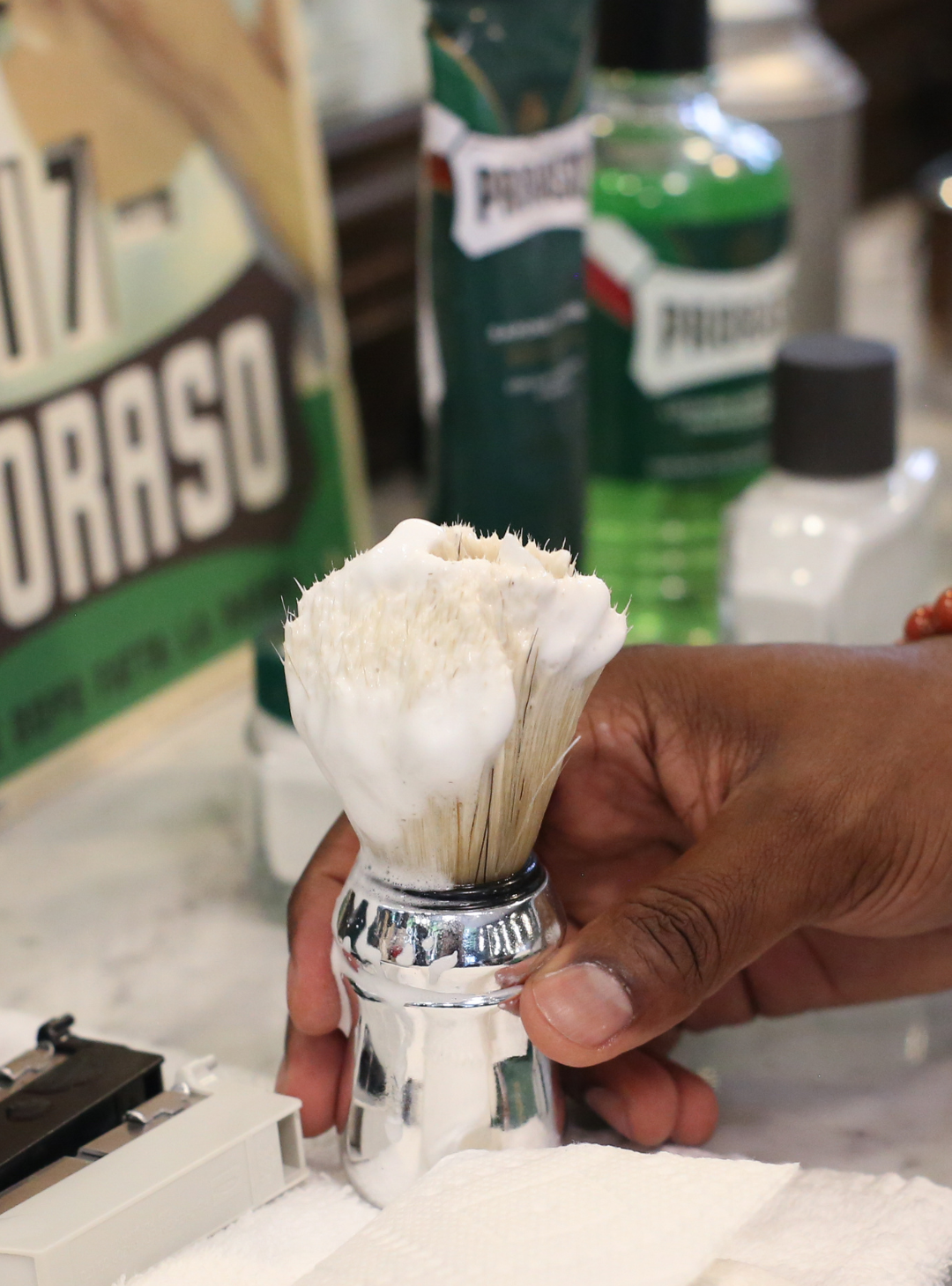 Barber reaching for a Professional Shave Brush that is loaded with shave cream on his station counter