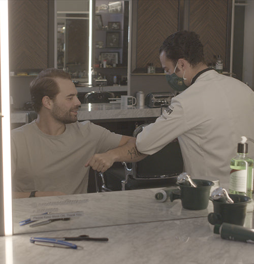 Proraso Master Barber Michael Haar elbow bumps client and friend Alec in front of the mirror at Haar & Co. Barbershop.
