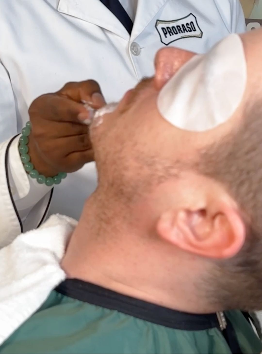 Man sitting in barber chair having Proraso Master Barber applying Pre-Shave Cream as the first step in a pro shave