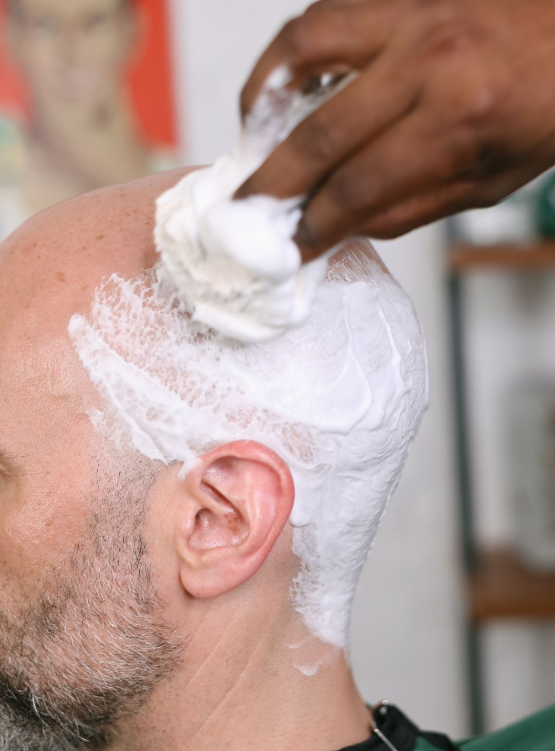 Closeup shot of a man's head with shave cream on it being lathered up by a barber holding a Professional Shave Brush