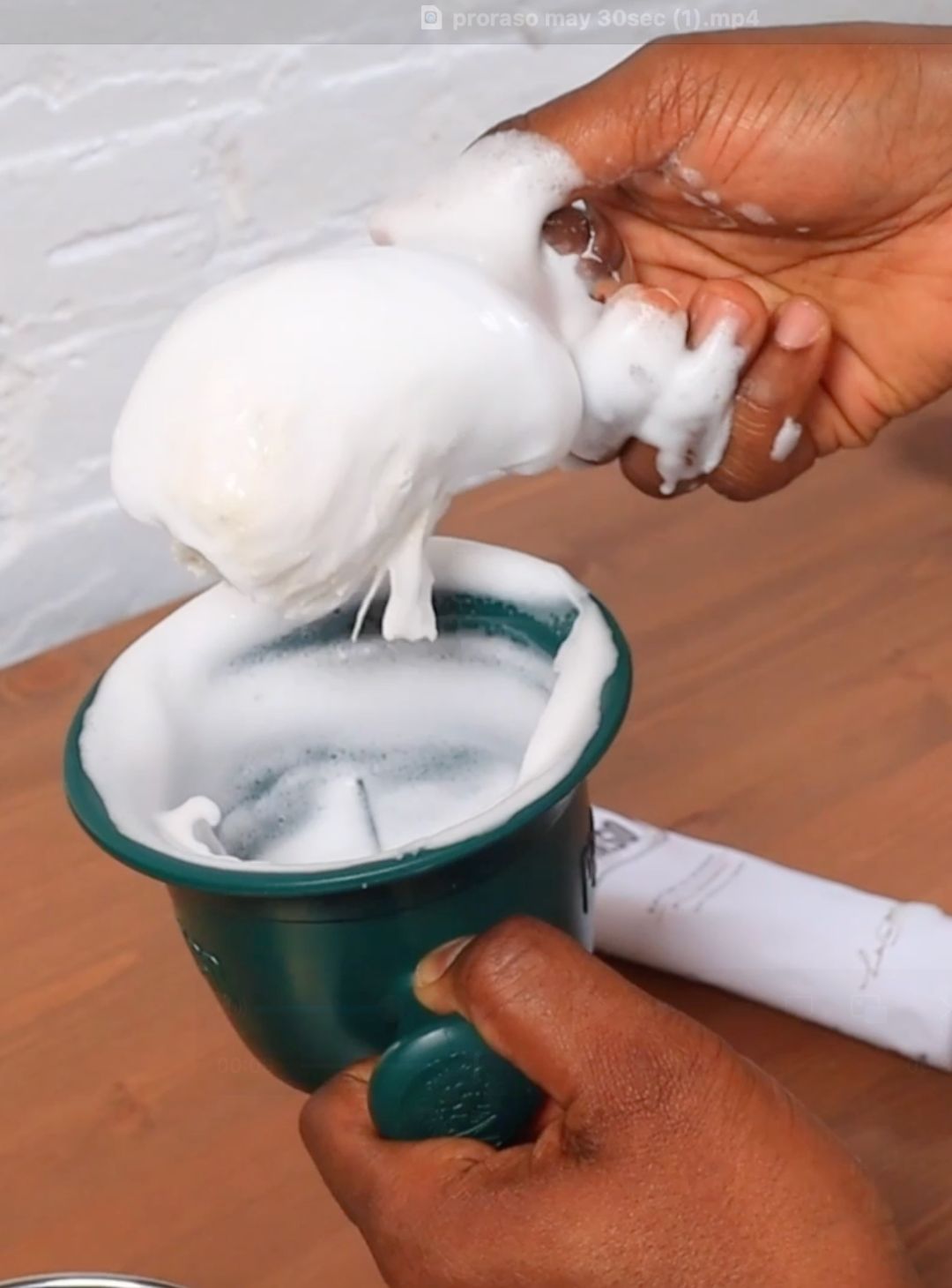 Proraso Master Barber creating a thick lather in a Proraso green shaving bowl with our Professional Shave Brush and Sensitive Shave Cream Tube sitting on a brown table
