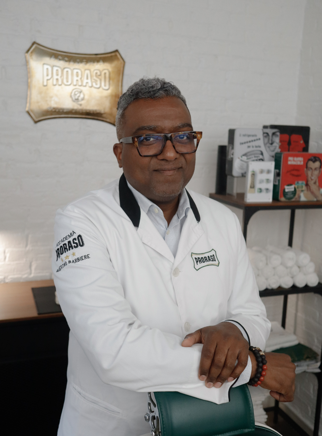 Image of Proraso Master Barber Sheldon Marcelle in the Proraso studio with vintage tins in the background resting his arm on a green barber chair