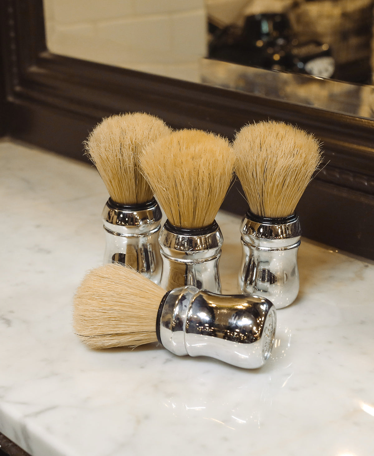 Group of four Professional Shave Brushes sitting on a white marble barbershop counter with mirror in background