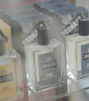 Proraso Wood & Spice Cologne, Cypress & Vetyver Cologne and Azur Lime Cologne on a glass shelf in a barber shop.
