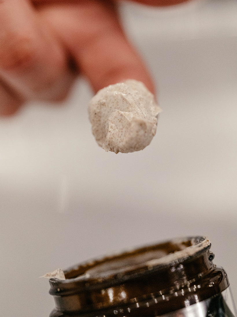 Finger scooping a larg dollop of Exfoliating Beard Paste and Facial Scrub, jar is visible at bottom of image