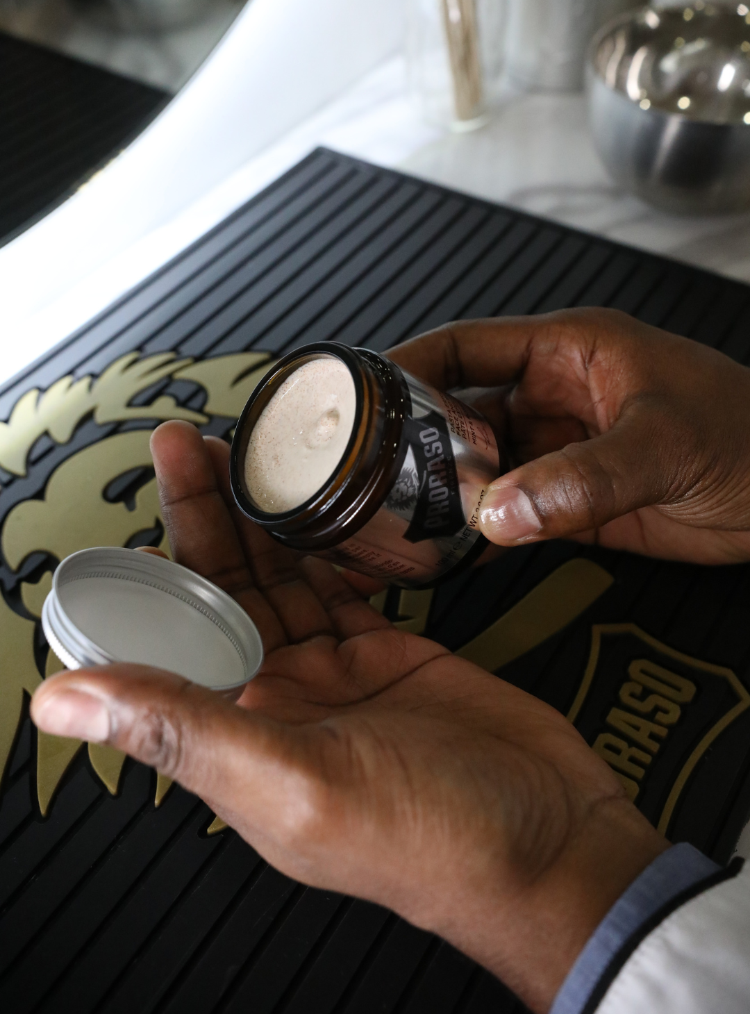 Proraso Master Barber opening a jar of Exfoliating Beard Paste & Facial Scrub on his station in a barber shop over a black rubber mat with Proraso logo