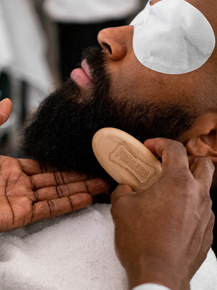 Barber using the Beard and Moustache Brush on a client reclined in a barber chair 