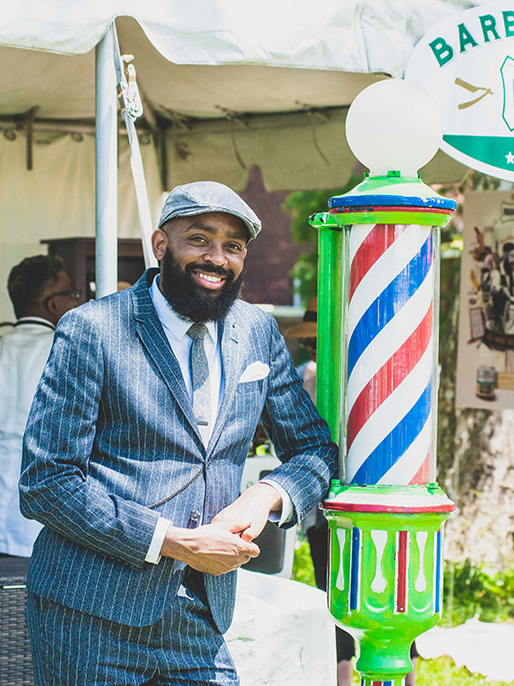 Proraso team member dressed in a suit standing in front of a vintage barber pole outside