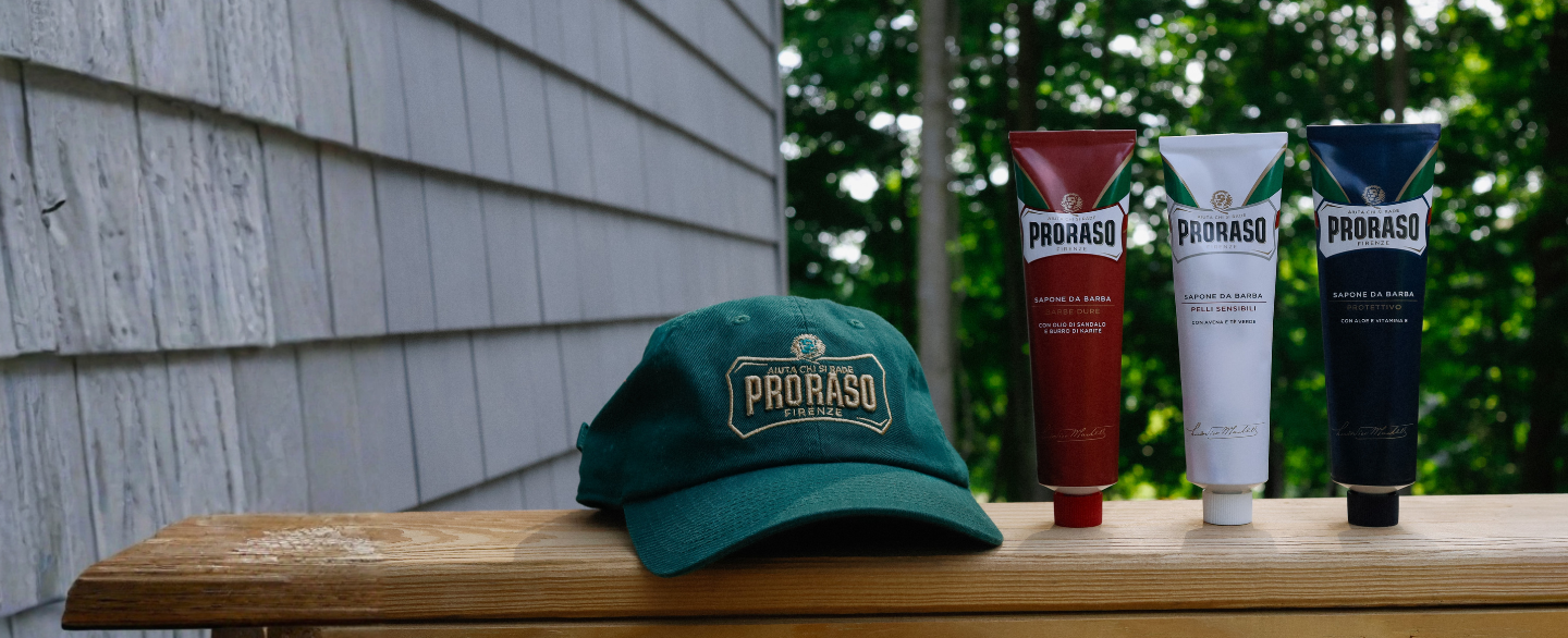 Proraso green logo cap sitting on a deck railing with our Red, White and Blue Shave Cream Tubes sitting next to it