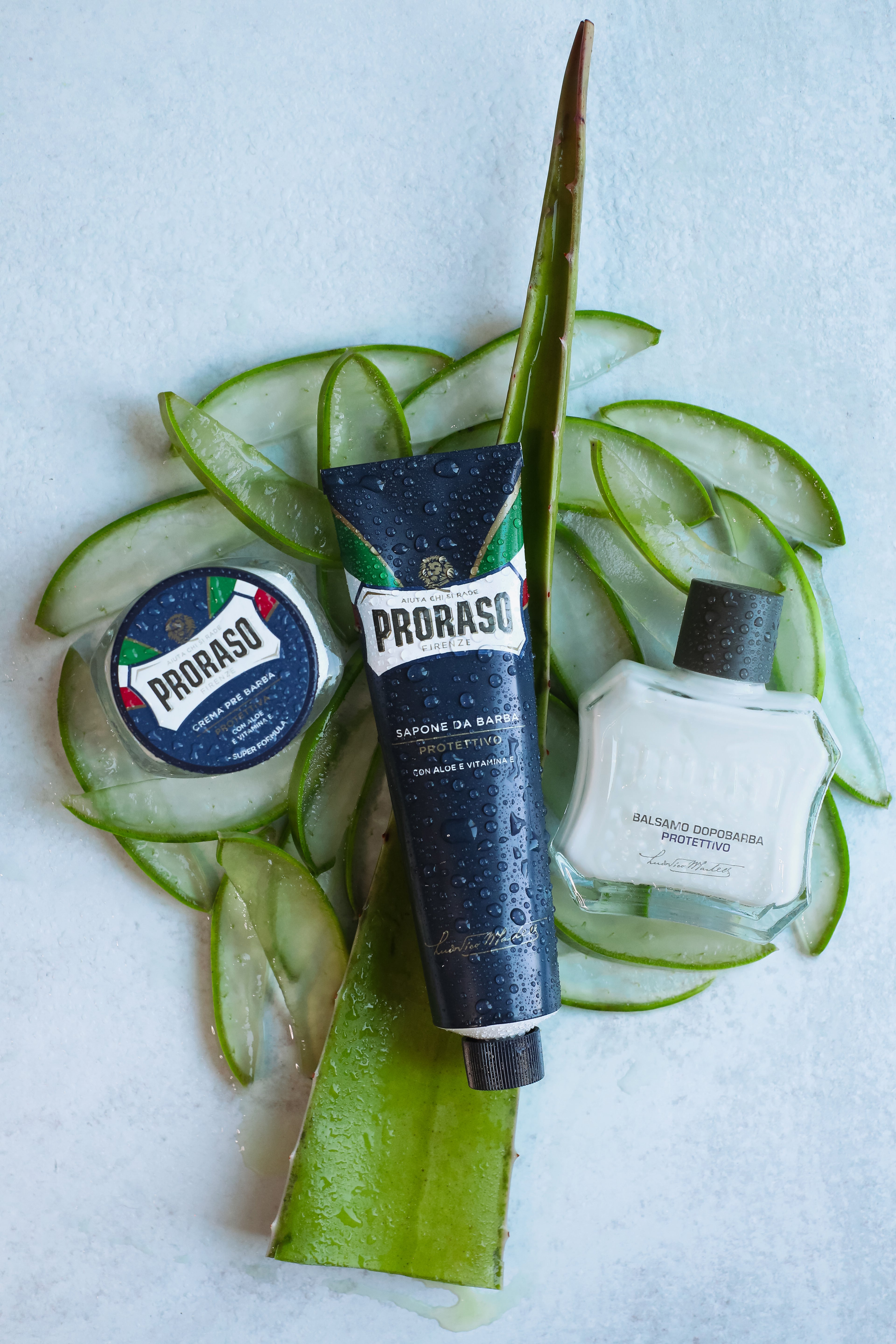Protective Formula Pre-Shave Cream, Shave Cream Tube and After Shave Balm on slices of aloe vera sitting on a grey table
