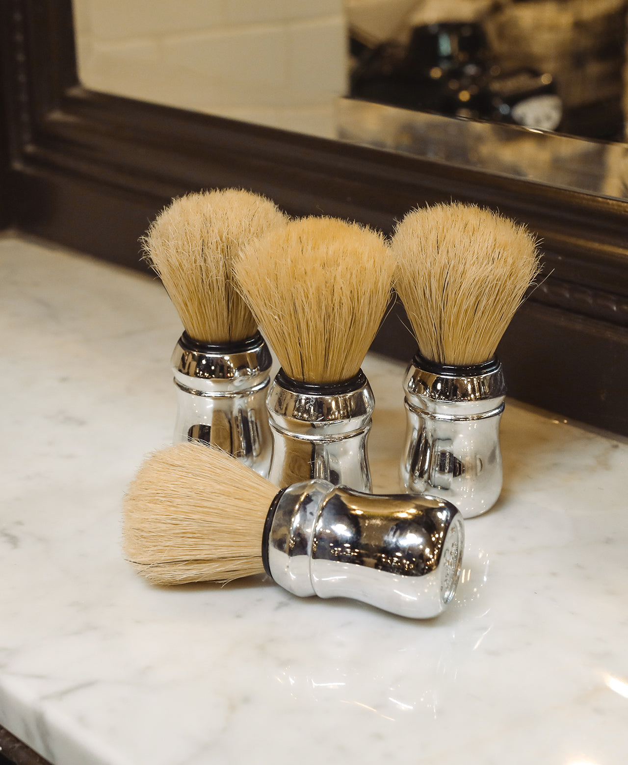 Group of four Professional Shave Brushes sitting on a white marble barbershop counter with mirror in background 