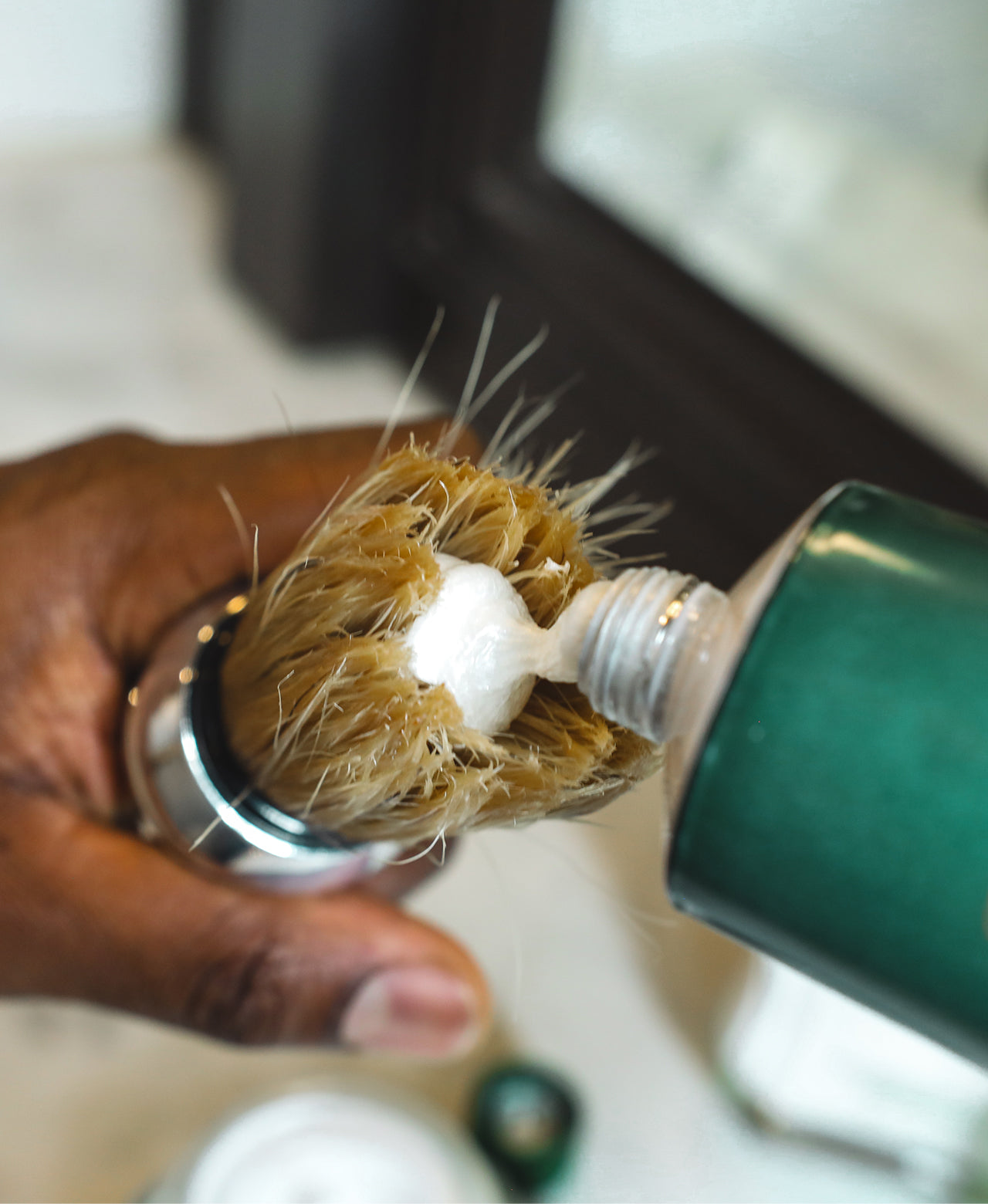 Professional Shave Brush in a man's hand with Refreshing Shave Cream Tube being squeezed in the bristles to make a lather 