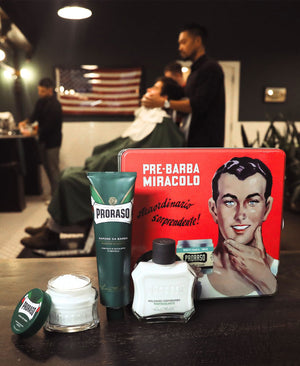 Vintage Gino Tin and contents, of Refreshing Pre-Shave Cream, Shave Cream Tube and After Shave Balm on a shelf in a barber shop with man in barber chair.