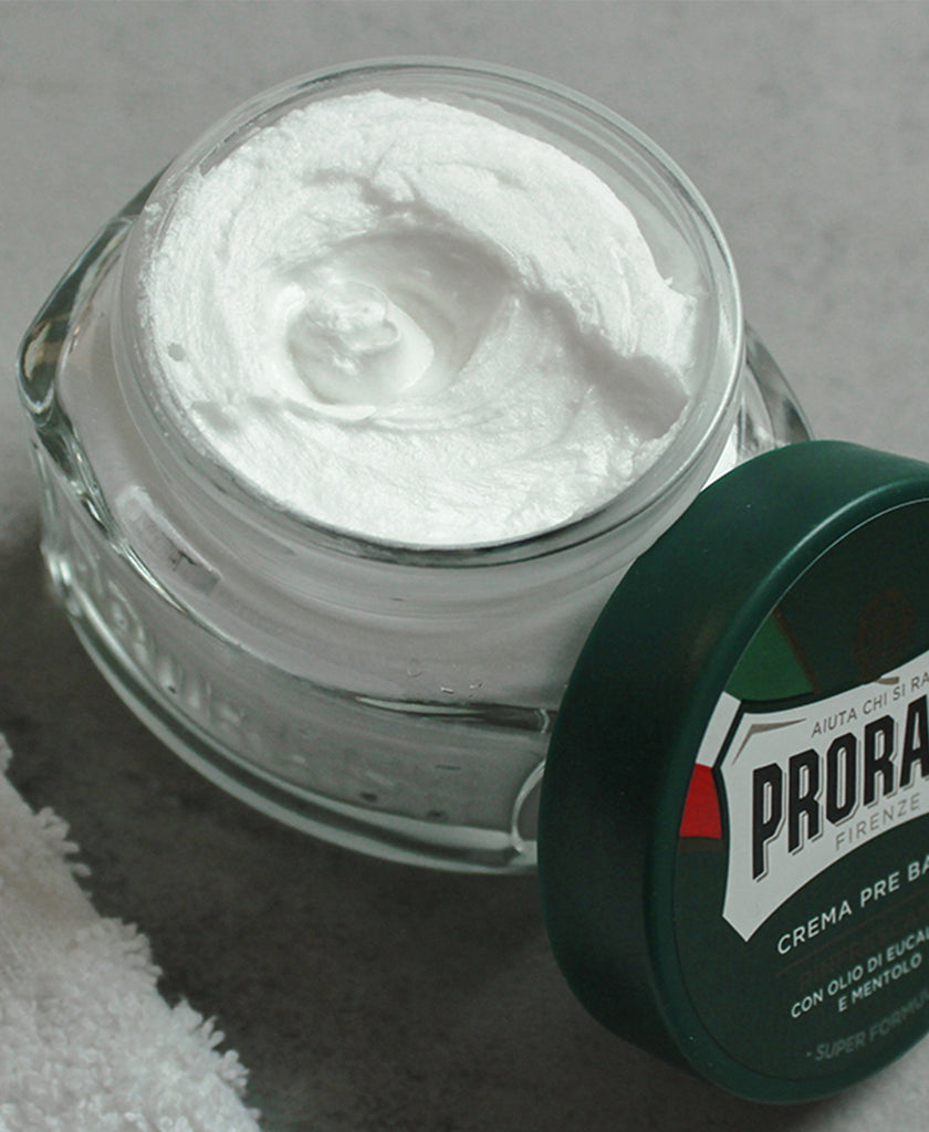 Refreshing Pre-Shave Cream jar with lid open to see thick texture with lid balanced on the side