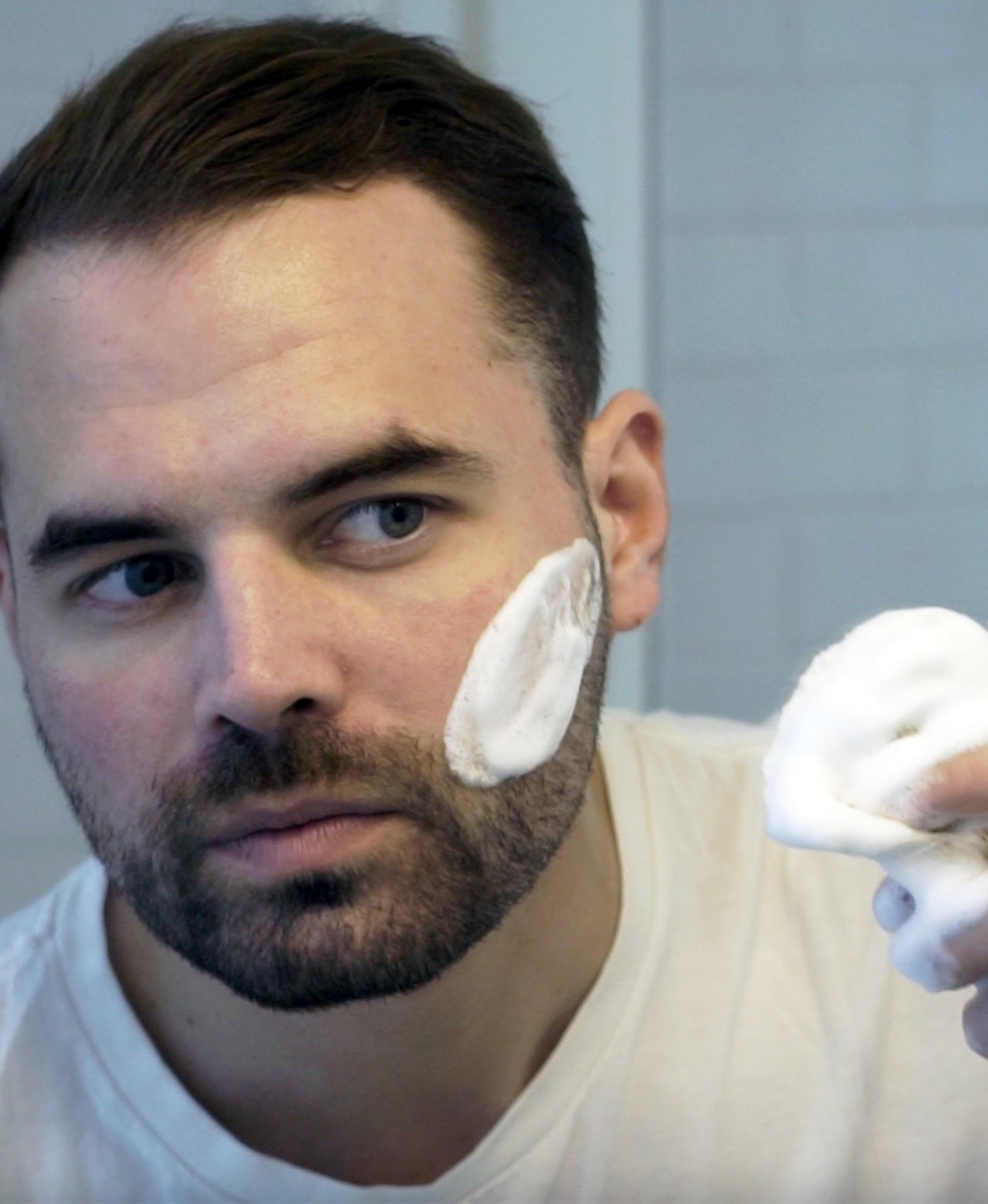 Man applying Sensitive Shave Cream Tube to face with a Professional Shave Cream Tube with white tile bathroom wall