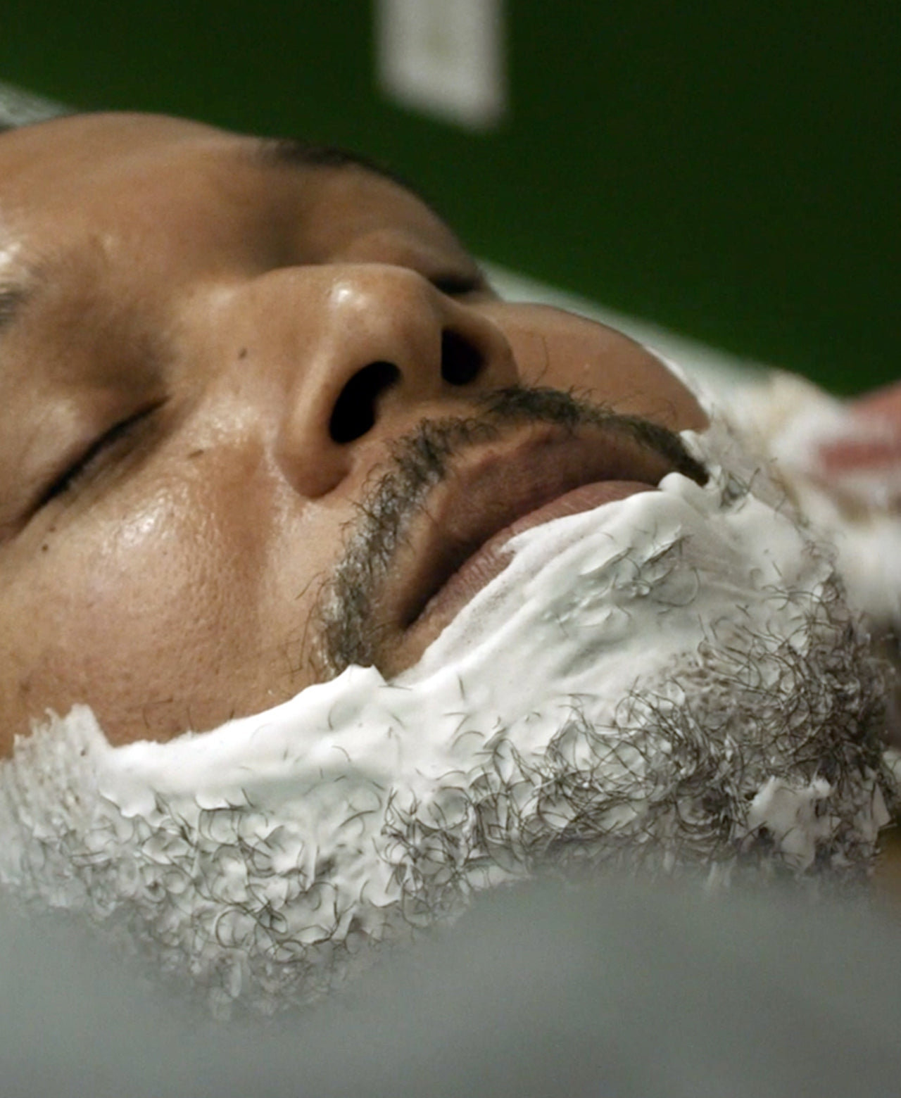 Man having thick lather applied to his face by a barber in the foreground 