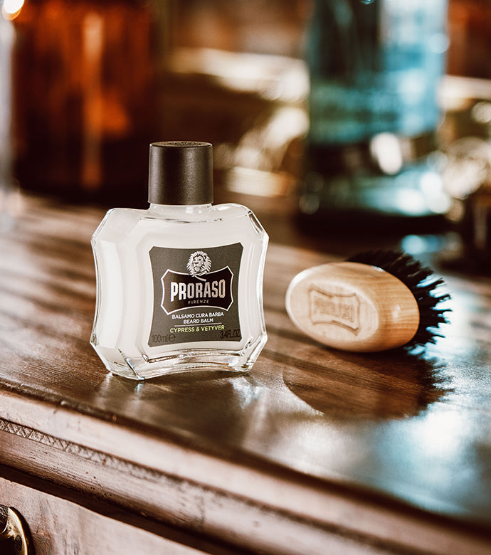 Cypress & Vetyver Beard Balm bottle on a wooden table sitting in front of a Moustache and Beard Brush