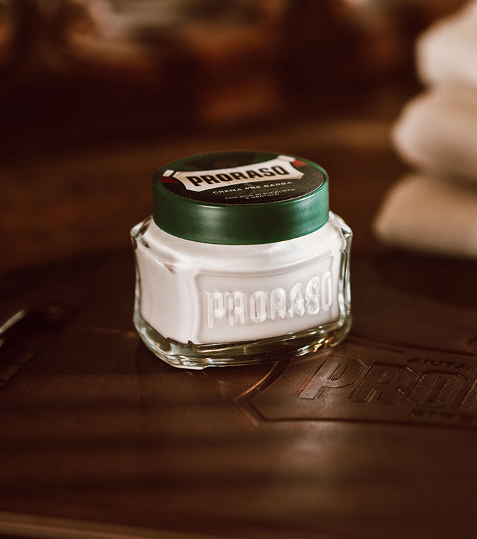 Refresh Pre-Shave Cream jar sitting on dark wood table with stacked white towels in background 