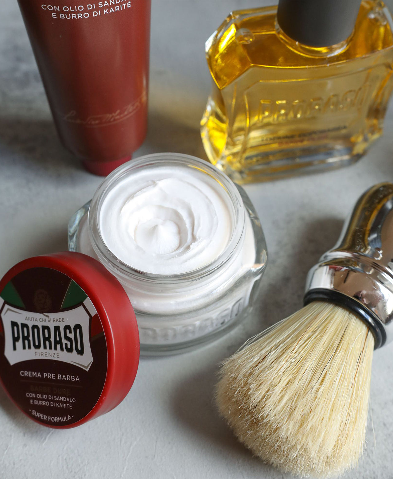 Coarse Beard Formula lineup sitting on grey table, from left to right Pre-Shave Cream with lid open showing thick texture, Shave Cream Tube, After Shave Lotion and Professional Shave Brush in the front