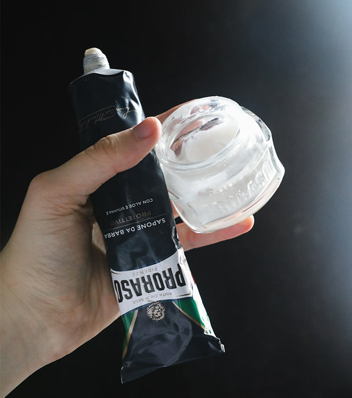 Protective Shave Cream tube and open jar of Pre-Shave Cream being held in a hand with a black background 