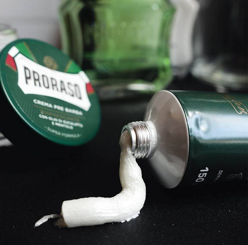 Refreshing Shave Cream Tube opened with shave cream squeezed out to show texture. The background shows a Refresh Pre-Shave Cream lid sitting on Pre-Shave Cream Jar with Refresh After Shave Lotion and After Shave Balm in background all sitting on a black marble table