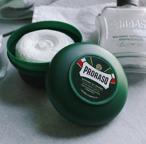 Refresh Shave Soap in a Bowl open with lid open to show texture, sitting next to a Refreshing After Shave Balm sitting on a grey counter with white towel in the background 