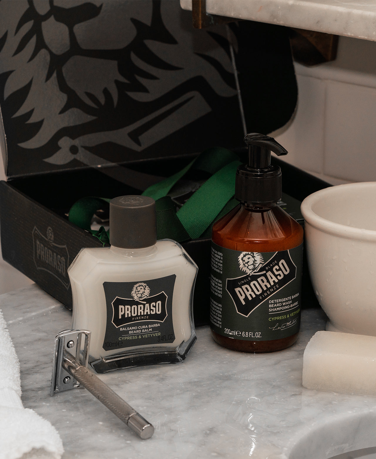 Cypress & Vetyver Beard Balm and Beard Wash with a silver double edge safety razor and Post-Shave Stone on white marble bathroom counter with Classic Beard Duo box open in the background