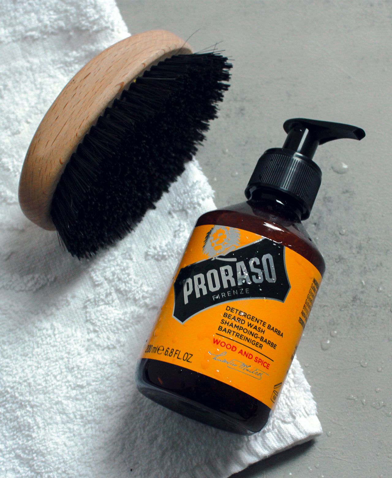 Bottle of Wood & Spice Beard Wash with an Old Style Military Brush on a grey table laying over a white towel