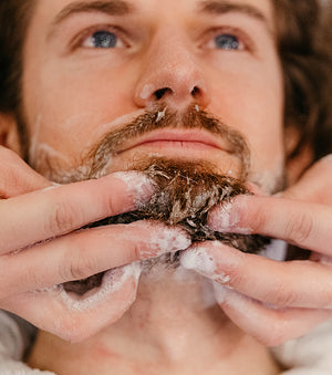 Photo of man having his bear washed, suds on his heard.