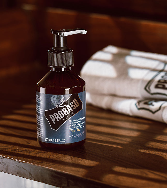 Azur Lime Beard Wash sitting on wooden barber counter with white Proraso towels folded in the background