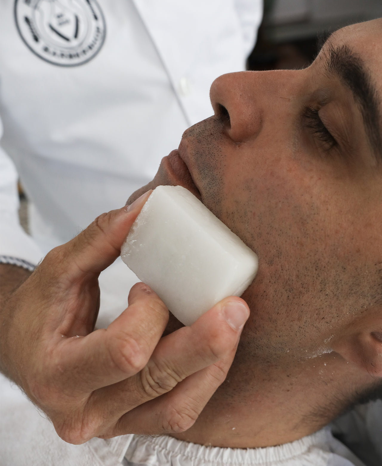 Client sitting in chair while barber holds Post-Shave Stone to face to end a shave