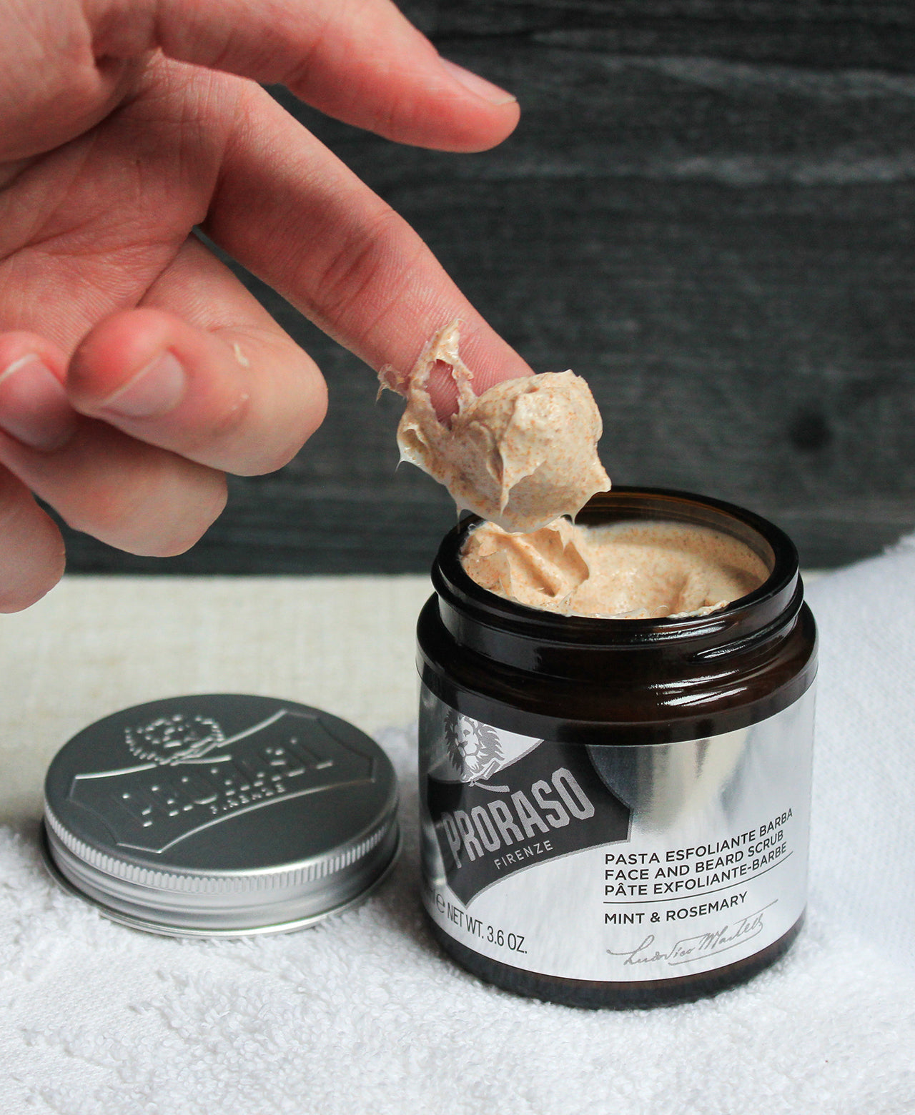 Hand finger with large scoop of Exfoliating Beard Scrub and Facial Scrub on finger from open jar of product