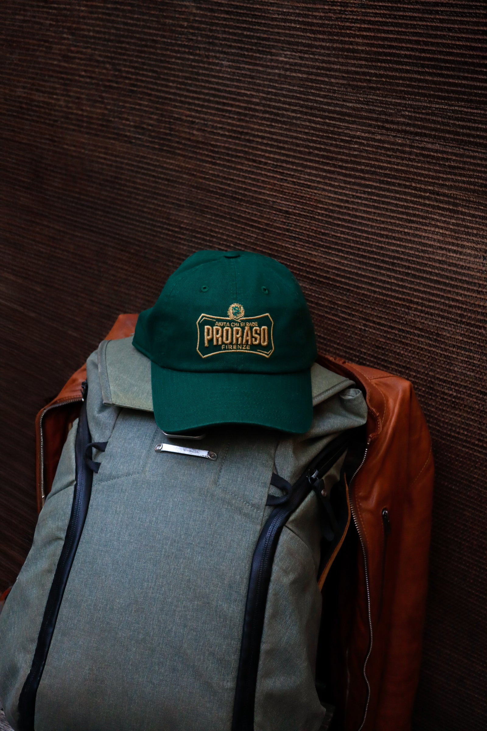 Proraso green cap with gold logo sitting on a grey backpack on a chair 