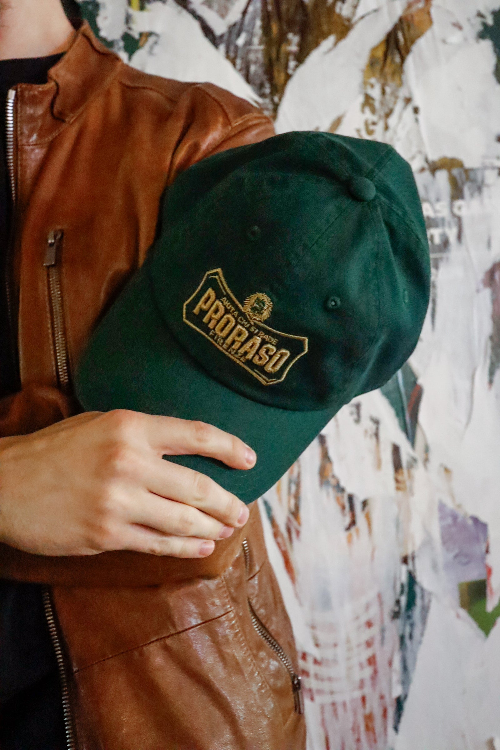 Proraso green cap with gold logo being held by man in front of his right arm wearing a leather jacket 