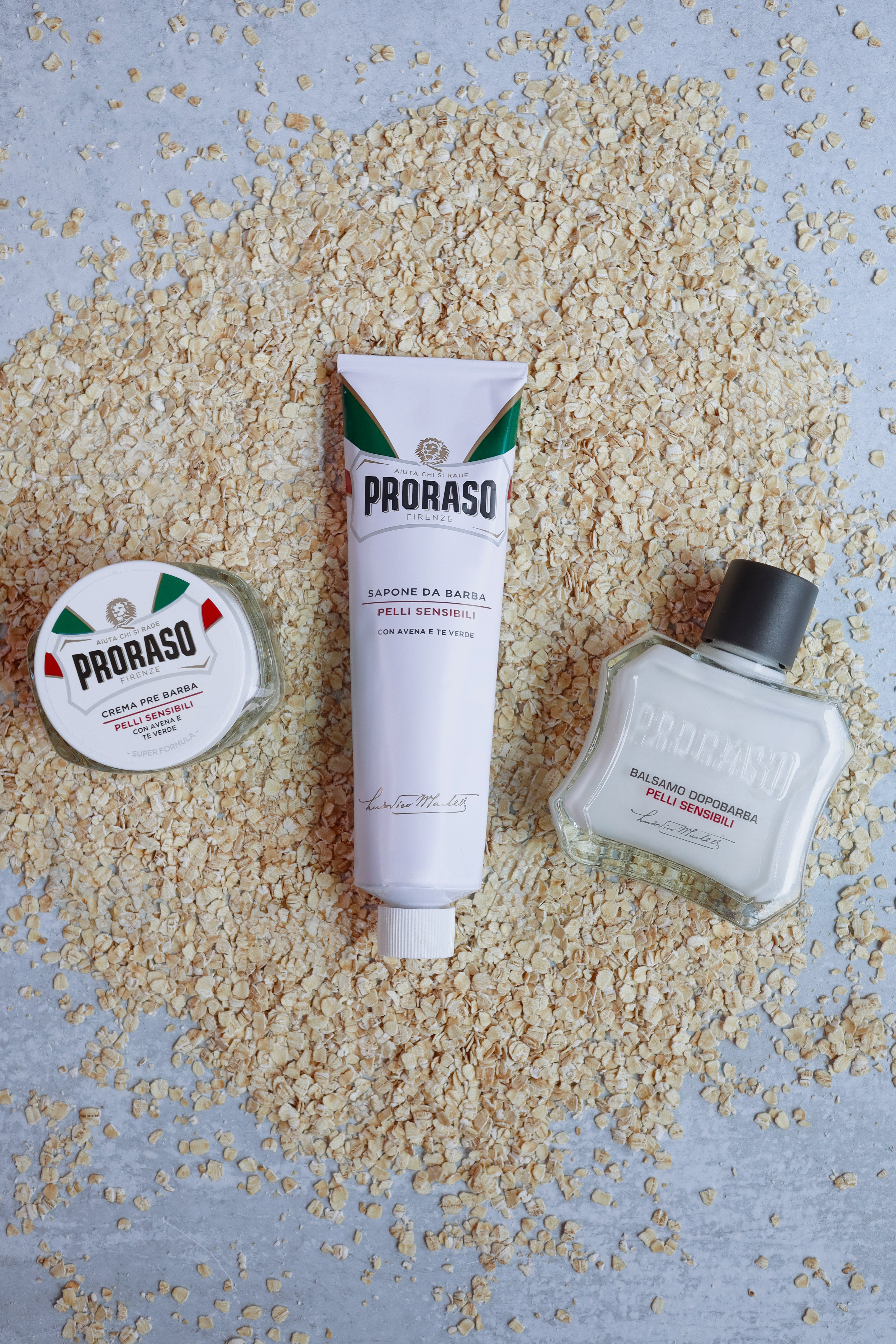 Sensitive Formula Pre-Shave Cream, Shave Cream Tube and After Shave Balm laying on oatmeal sitting on a grey table