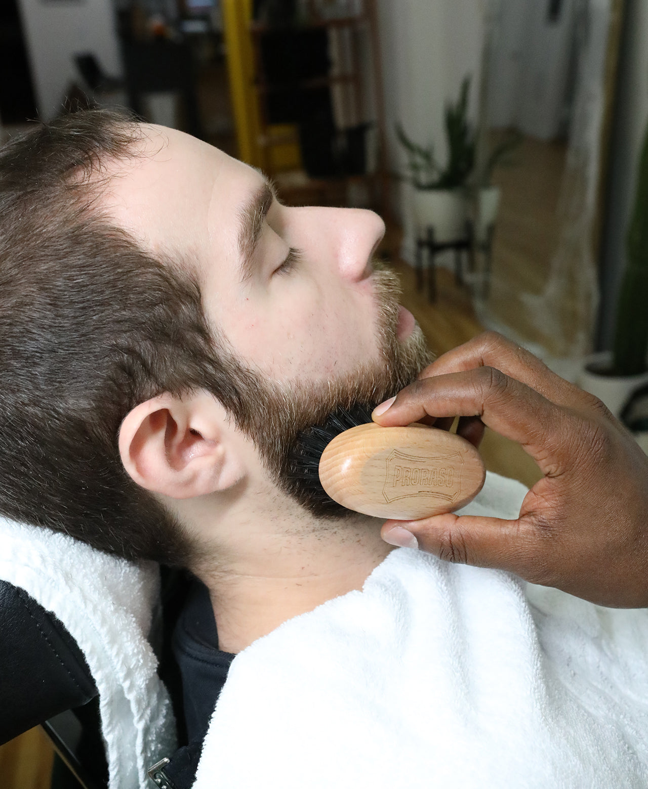 Man with a short beard with a barber using the Moustache and Beard Brush on his beard in a barbershop 