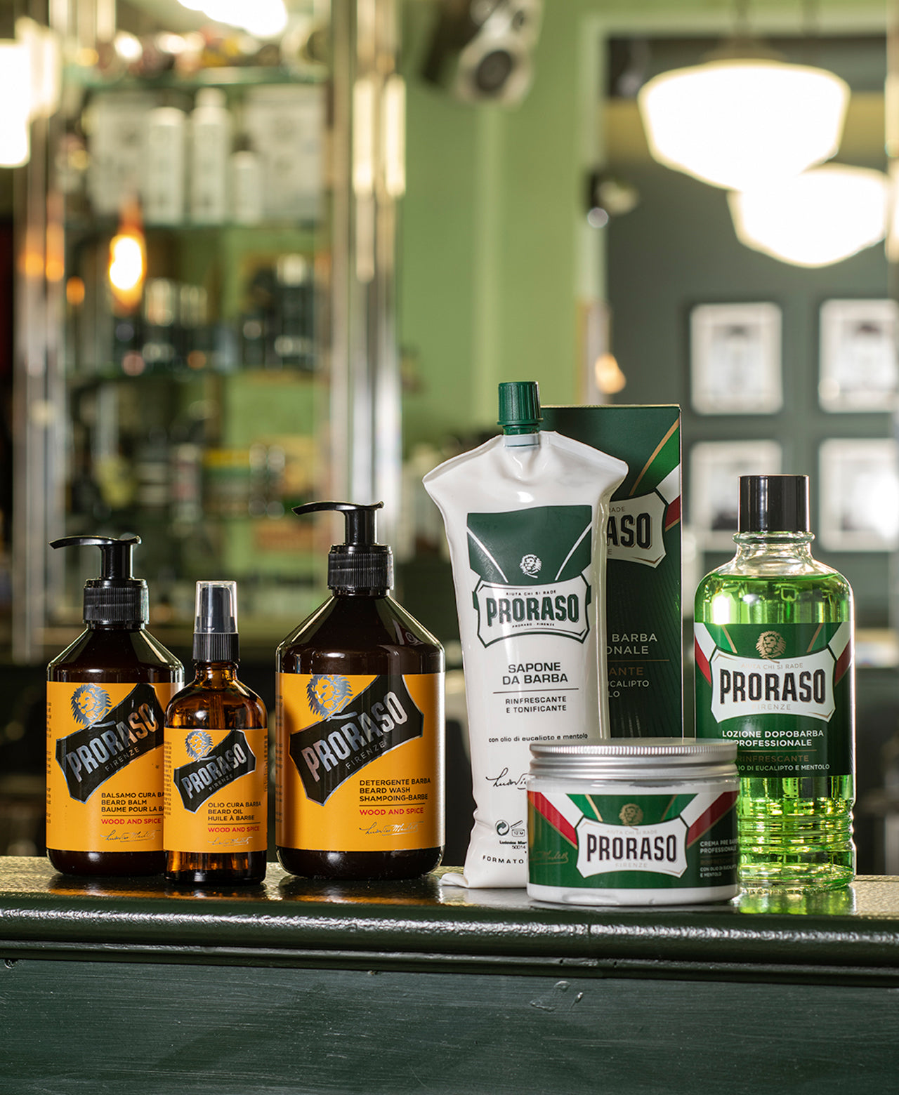 Professional size lineup from left to right Wood & Spice Beard Balm, Beard Oil and Beard Wash, Refresh Shave Cream, Pre-Shave Cream and After Shave Lotion sitting on a green shelf in a green barbershop