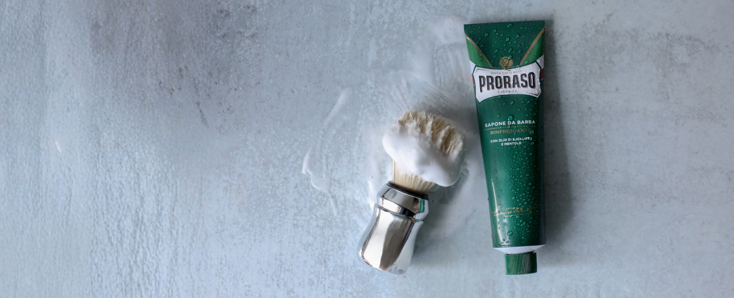 Proraso Professional Shave Brush with Shave Cream Tube lather on it next to a tube of Refresh Shave Cream Tube on a grey table