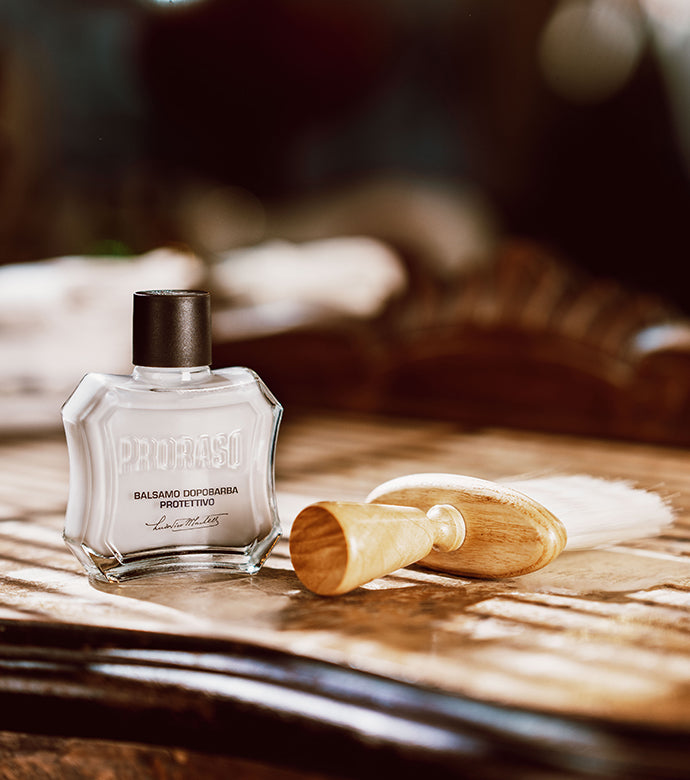 Protective After Shave Balm bottle with Barber Brush sitting on dark wood table.