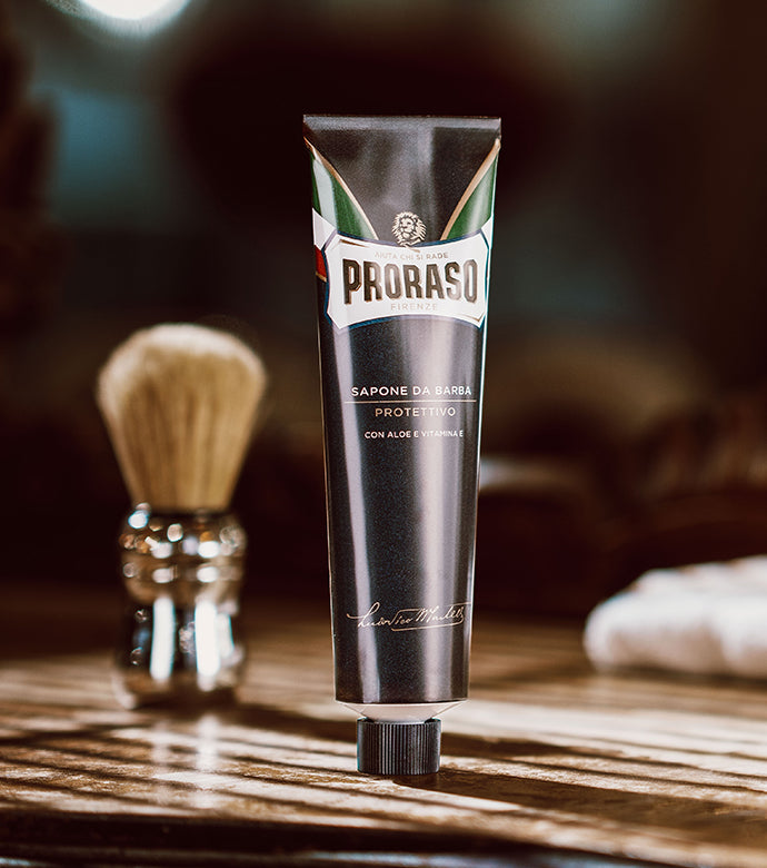 Protective Shave Cream Tube sitting on dark brown wood table with Professional Shave Brush and white barber towel in background 