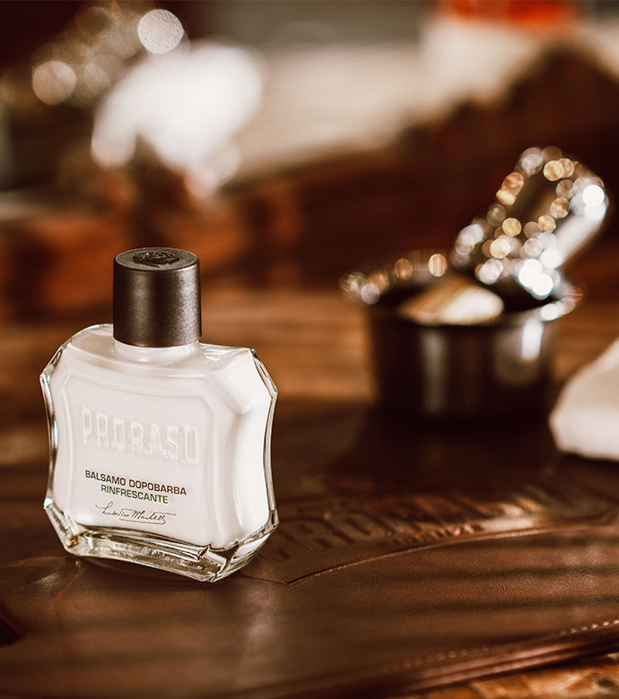 Refreshing After Shave Balm bottle sitting on a brown table with a Professional Shave Brush in a mug in the background 