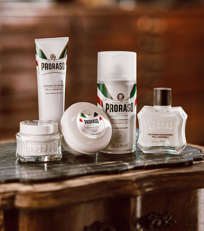 Sensitive Shave Formula lineup left to right: Pre-Shave Cream, Shave Cream Tube, Shaving Soap in a Bowl, Shave Foam and After Shave Balm sitting on a dark brown table