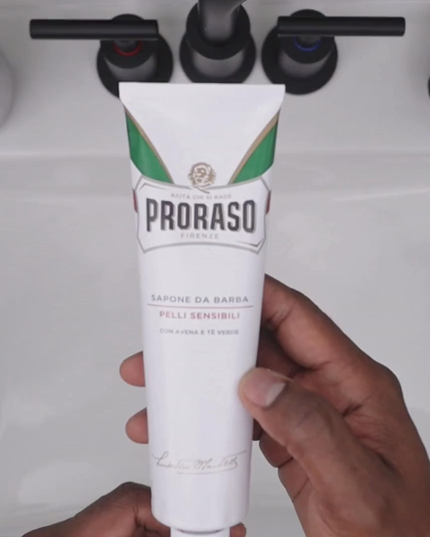 Man building lather with Shave Cream Tube for Sensitive Skin and Professional Shave Brush in a bowl over a sink
