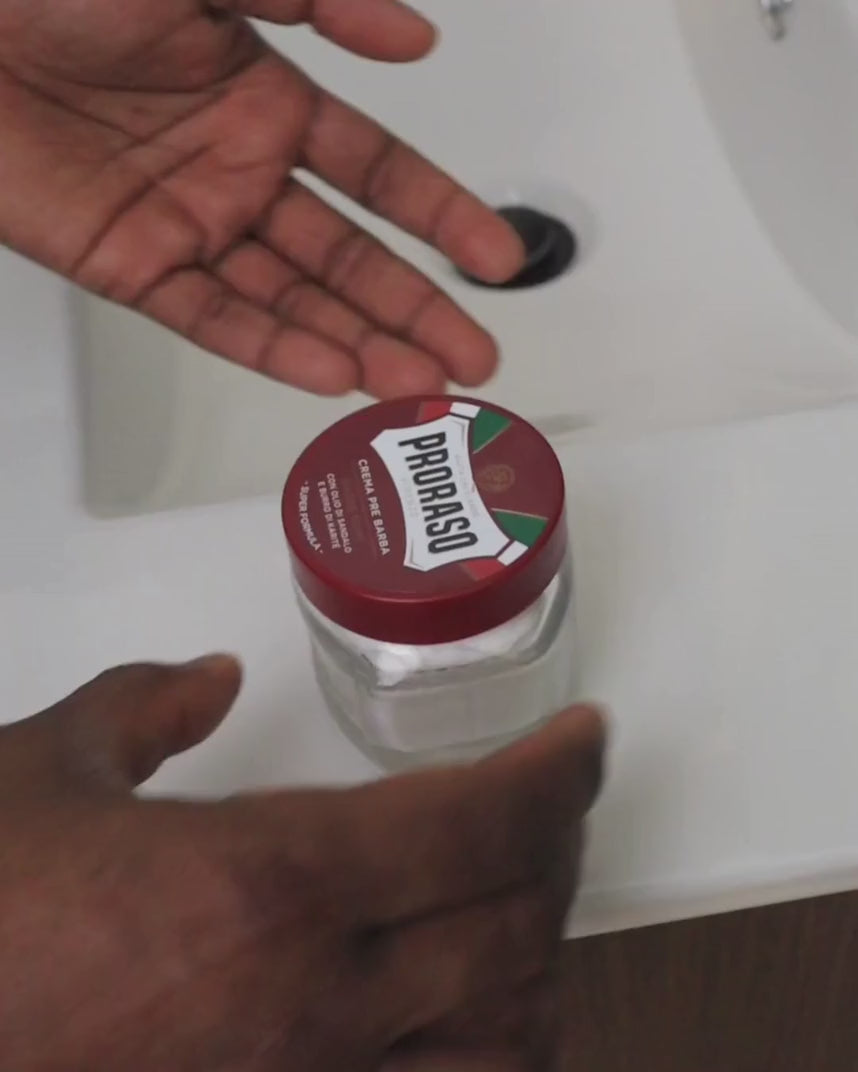 Man opening and scooping out Pre-Shave Cream for Coarse Beards at bathroom sink
