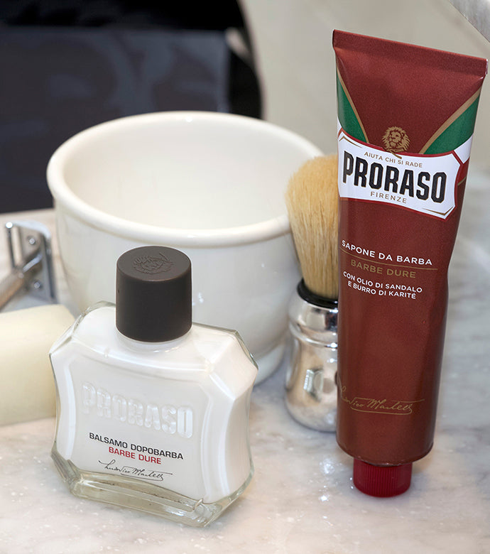 Proraso Post-Shaving Stone, Proraso Nourishing for Coarse Beards After Shave Balm, Proraso Professional Shave Brush and Proraso Nourishing Shave Cream Tube with Shave Bowl on bathroom counter.
