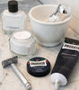 Proraso Protective Line on bathroom counter: Proraso Protective Aftershave Balm, Proraso Protective Pre-Shave Cream with lid off, Proraso Protective Shaving Cream Tube with cream squeezed out, with a safety razor, shave bowl and Proraso Professional Shaving Brush.