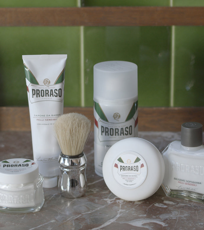 Proraso Sensitive Shaving Lineup: Pre-Shave Cream, Shaving Cream Tube, Professional Shave Brush, Shave Foam, Shaving Soap in a Bowl and After Shave Balm on counter.