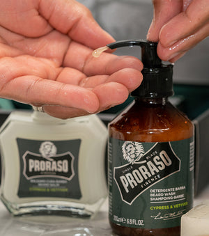 Proraso Cypress & Vetyver Beard Wash being pumped into hand with Proraso Cypress & Vetyver Beard Balm in background on bathroom counter.