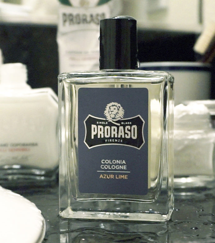 Proraso Azur Lime Cologne sitting on the side of a bathroom sink with After Shave Balm and Shaving Cream Tube in the background.