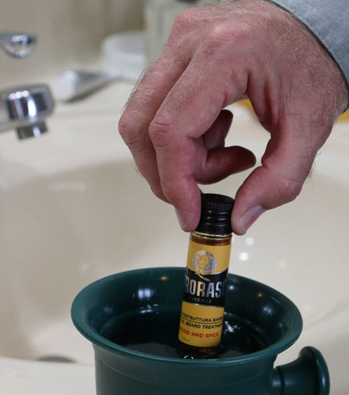 Proraso Hot Oil Beard Treatment: Wood & Spice being immersed in shave mug of hot water with hand.